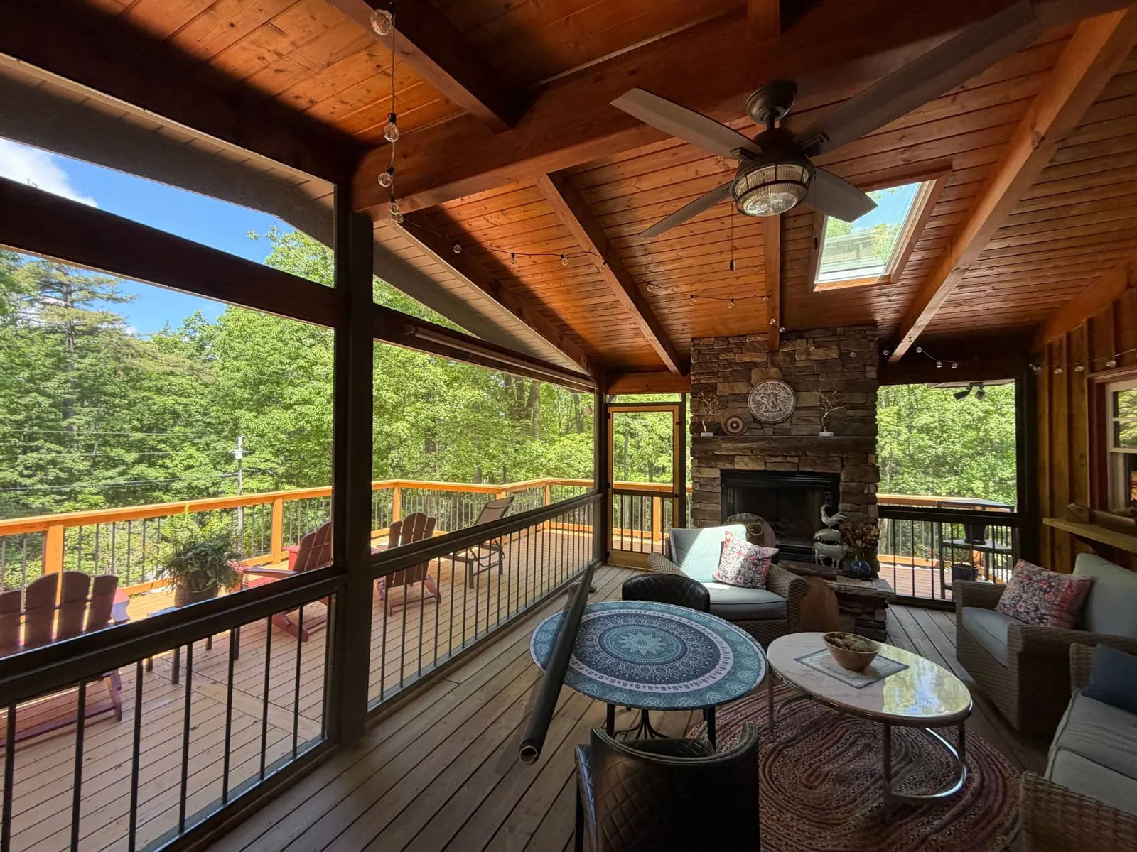 Screened porch with a stained tongue-and-groove ceiling, stone fireplace and a view of a new deck in Cashiers, North Carolina