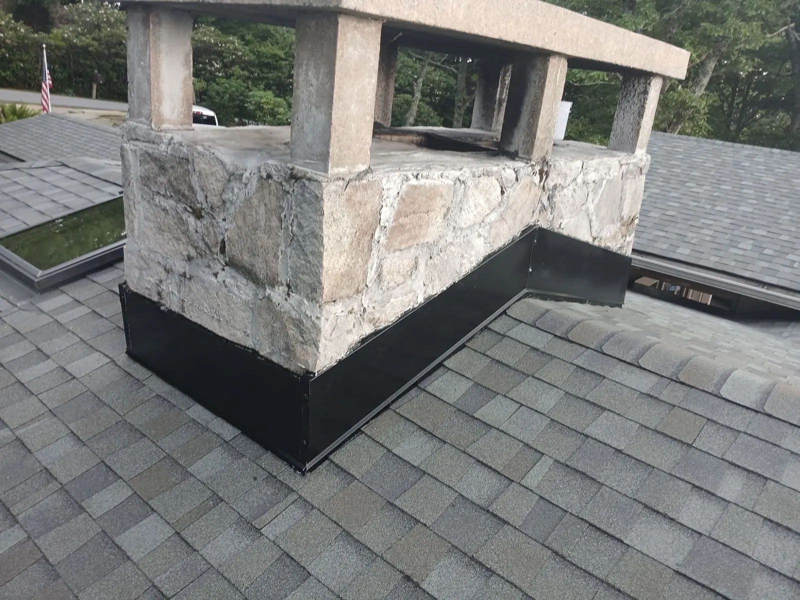 Stone chimney wrapped in new black metal counter-flashing on a shingle roof