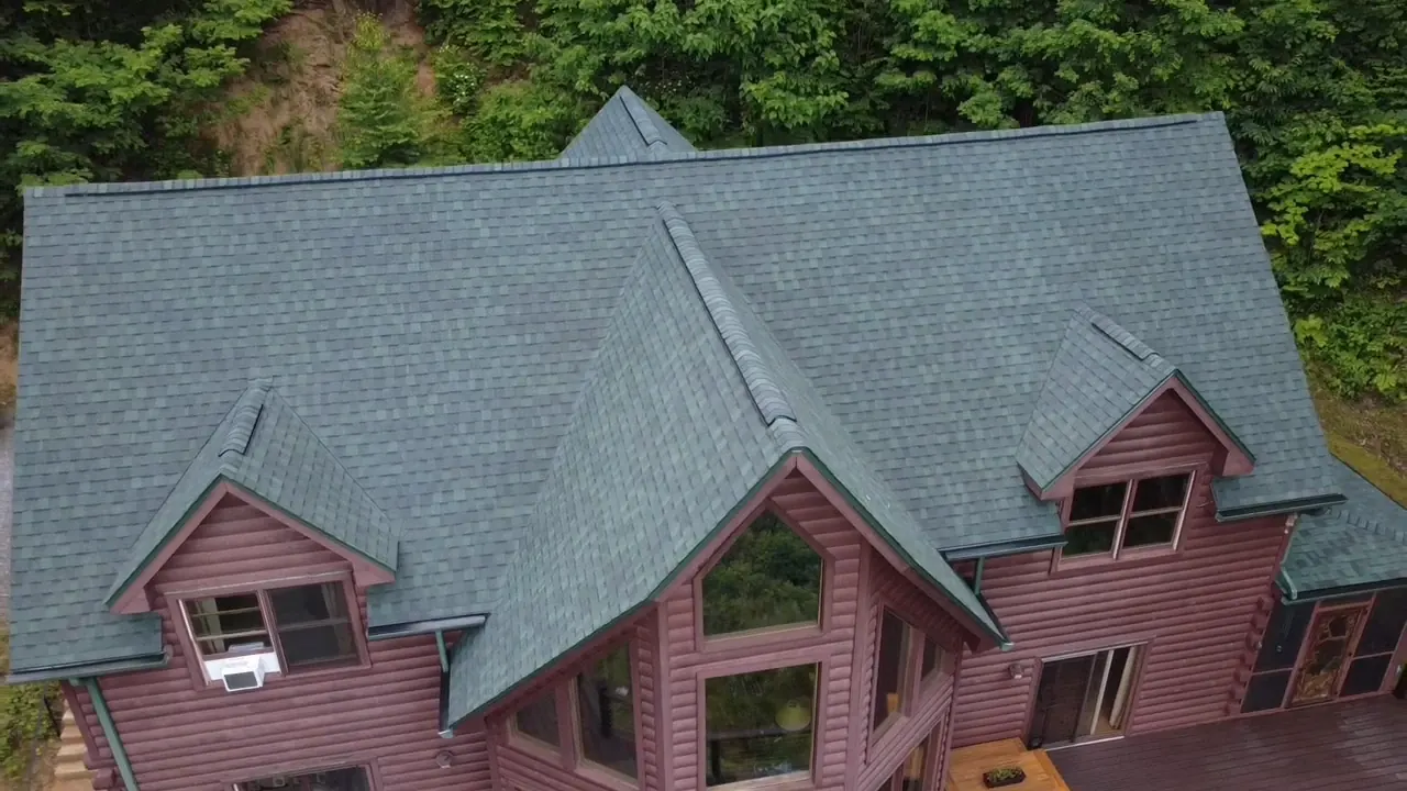 Green dimensional shingle roof with three gables on a red log home