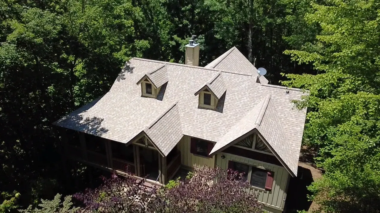 Light tan dimensional shingle roof with two dormers on a wooded mountain cottage