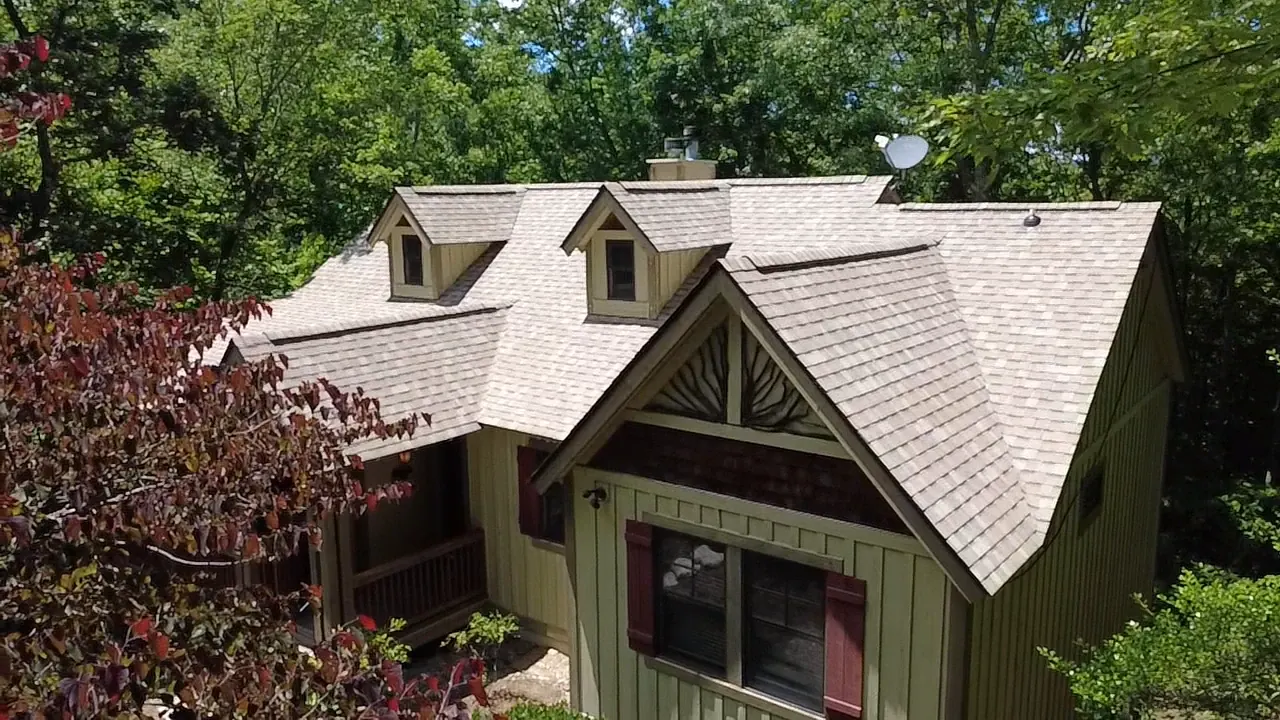 Light tan dimensional shingle gable and dormers on a green board-and-batten cottage